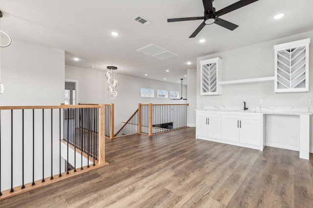 interior space with white cabinetry, hardwood / wood-style floors, hanging light fixtures, ceiling fan with notable chandelier, and sink