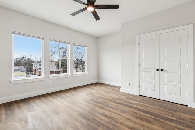 unfurnished bedroom with ceiling fan, multiple windows, a closet, and hardwood / wood-style floors