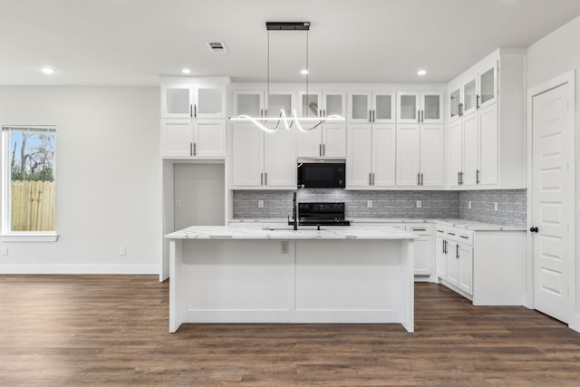 kitchen featuring light stone countertops, white cabinetry, pendant lighting, and an island with sink