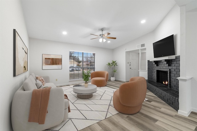 living room with ceiling fan, light hardwood / wood-style flooring, a fireplace, and lofted ceiling