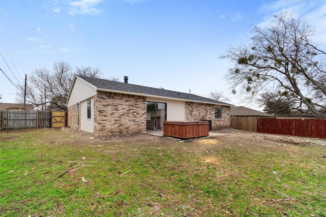 back of house with a hot tub and a lawn