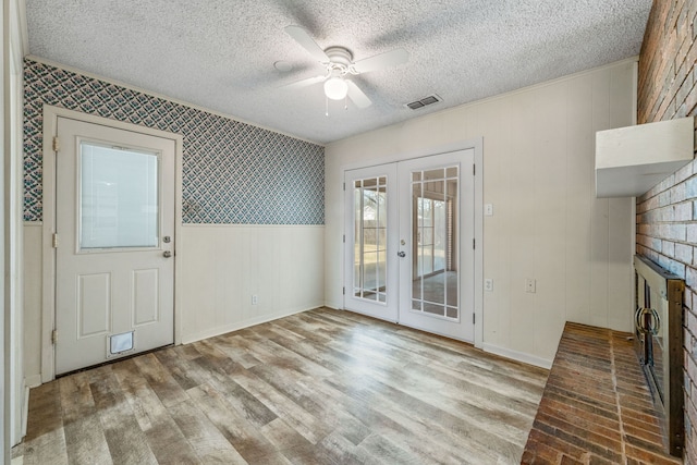 interior space with ceiling fan, a textured ceiling, french doors, and a fireplace