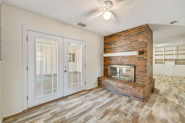 unfurnished living room featuring a textured ceiling, a brick fireplace, light wood-type flooring, french doors, and ceiling fan