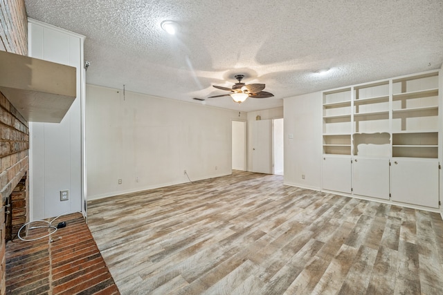 unfurnished living room with ceiling fan, a brick fireplace, light hardwood / wood-style floors, and a textured ceiling