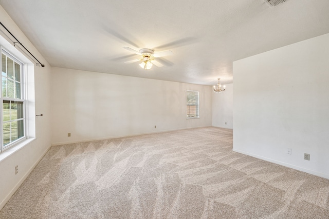 carpeted empty room featuring plenty of natural light and ceiling fan with notable chandelier