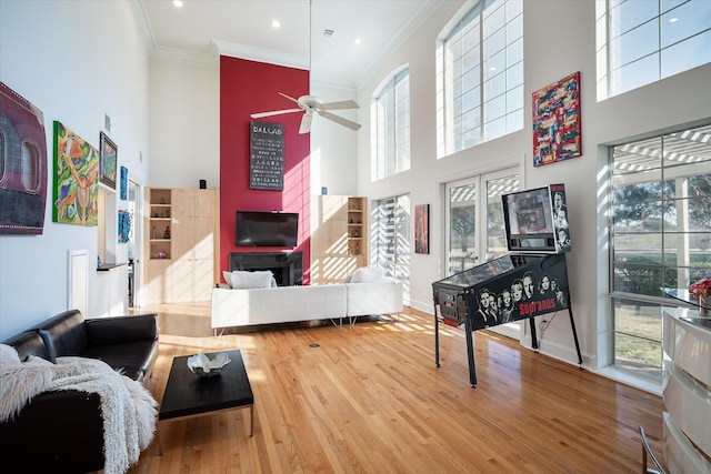 living room with hardwood / wood-style flooring, a towering ceiling, ornamental molding, and ceiling fan