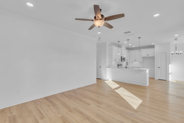 unfurnished living room featuring sink, ceiling fan with notable chandelier, light hardwood / wood-style flooring, and crown molding