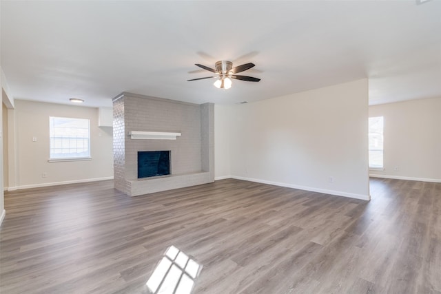 unfurnished living room featuring ceiling fan, a brick fireplace, and hardwood / wood-style floors