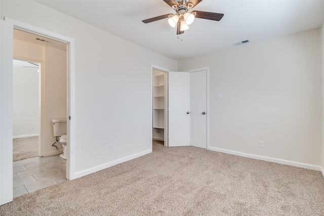 unfurnished bedroom with a walk in closet, light carpet, a closet, ceiling fan, and ensuite bathroom