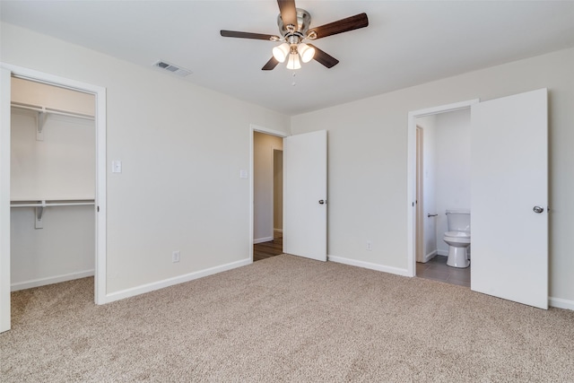 unfurnished bedroom featuring a spacious closet, ensuite bath, a closet, carpet flooring, and ceiling fan