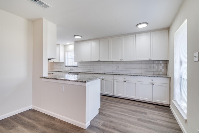 kitchen featuring white cabinetry, decorative backsplash, kitchen peninsula, light stone counters, and light hardwood / wood-style flooring