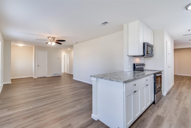 kitchen with light stone countertops, white cabinets, appliances with stainless steel finishes, decorative backsplash, and light wood-type flooring