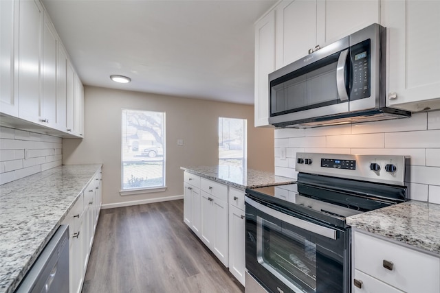 kitchen featuring appliances with stainless steel finishes, white cabinetry, light hardwood / wood-style floors, decorative backsplash, and light stone counters