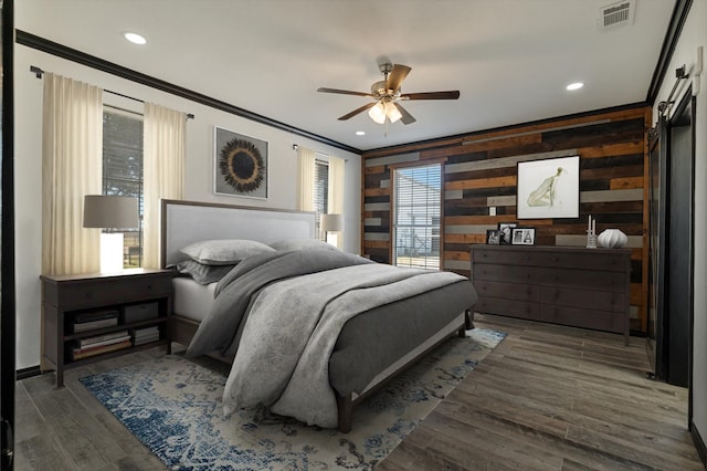 bedroom featuring dark hardwood / wood-style floors, wood walls, ceiling fan, crown molding, and a barn door