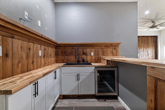 bar featuring ceiling fan, sink, white cabinetry, butcher block counters, and beverage cooler