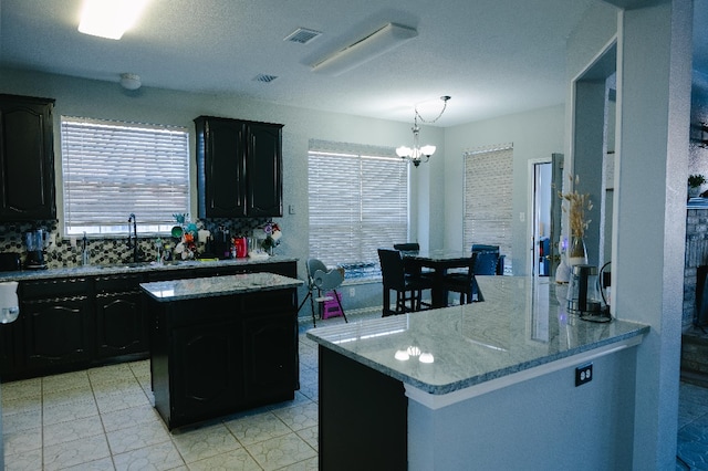 kitchen with a center island, tasteful backsplash, sink, a chandelier, and light stone counters