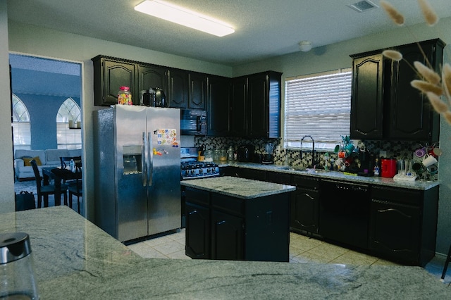 kitchen featuring light stone countertops, black appliances, a kitchen island, decorative backsplash, and sink