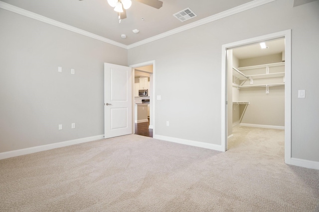 unfurnished bedroom featuring a walk in closet, light carpet, a closet, ceiling fan, and crown molding