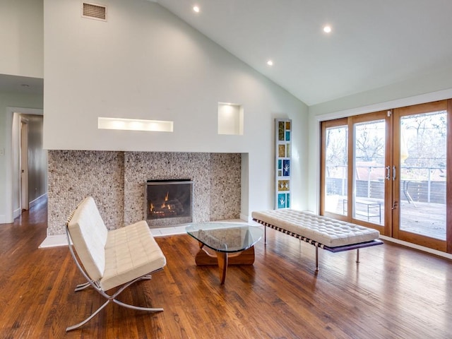 living area with high vaulted ceiling, wood-type flooring, and a tiled fireplace