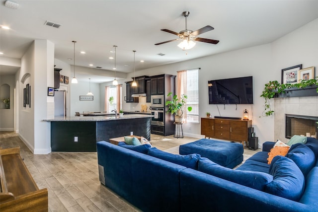 living room featuring sink, a tiled fireplace, and ceiling fan