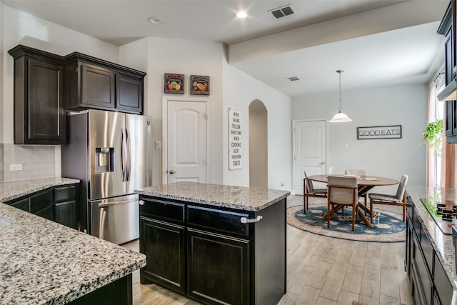 kitchen featuring a center island, tasteful backsplash, light hardwood / wood-style floors, stainless steel fridge, and light stone counters