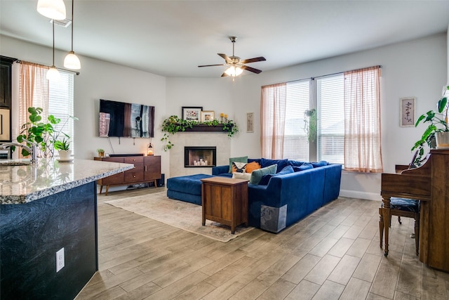 living room with light hardwood / wood-style floors, sink, ceiling fan, and a tiled fireplace