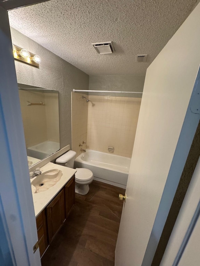 full bathroom with a textured ceiling, tiled shower / bath combo, vanity, toilet, and hardwood / wood-style flooring