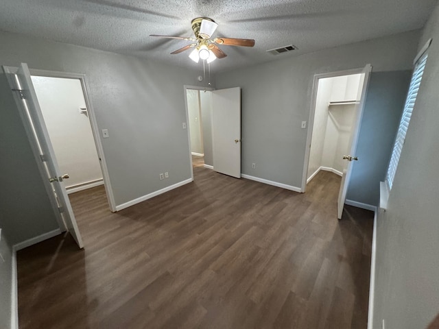 unfurnished bedroom with a spacious closet, a textured ceiling, a closet, dark hardwood / wood-style flooring, and ceiling fan