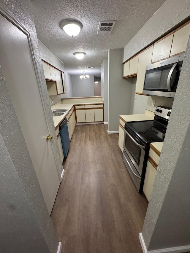 kitchen with appliances with stainless steel finishes, sink, a textured ceiling, light hardwood / wood-style floors, and an inviting chandelier