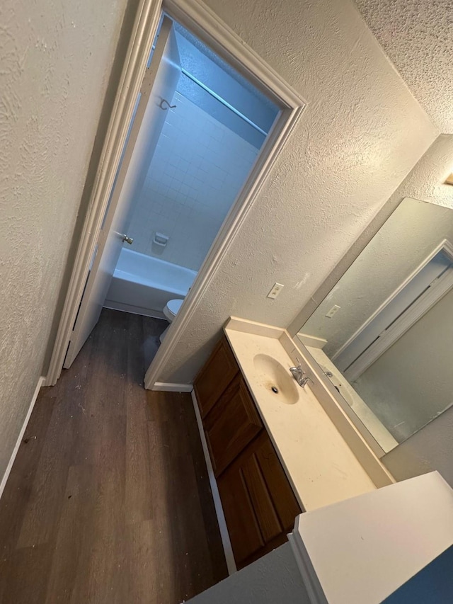 full bathroom featuring wood-type flooring, tub / shower combination, toilet, a textured ceiling, and vanity