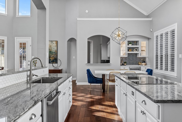 kitchen featuring sink, black electric cooktop, dark stone countertops, and an island with sink