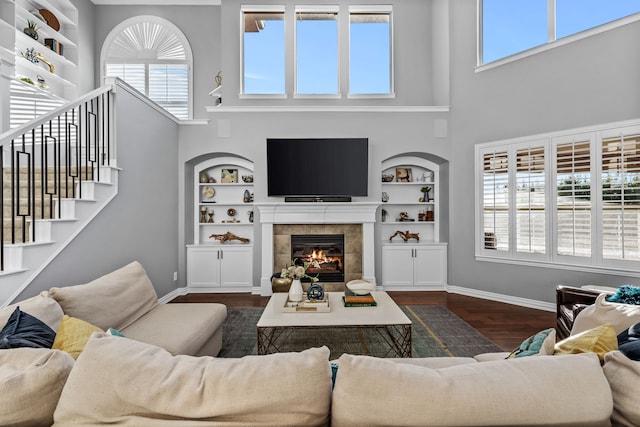 living room with a high ceiling, dark wood-type flooring, built in shelves, and a tiled fireplace