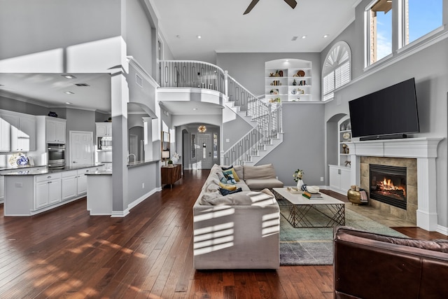 living room with ceiling fan, built in shelves, a tile fireplace, and dark hardwood / wood-style flooring