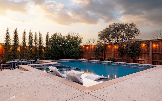 pool at dusk featuring an in ground hot tub and a patio area