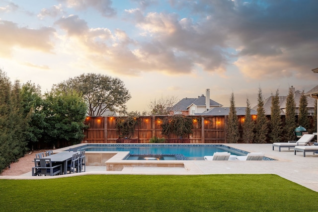 pool at dusk with an in ground hot tub, a patio, and a yard