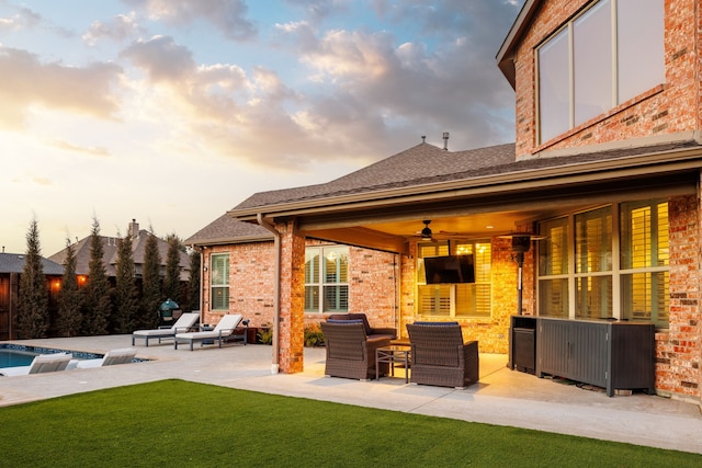 back house at dusk featuring ceiling fan, a patio area, a yard, and an outdoor living space