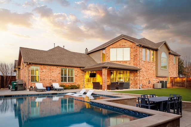 back house at dusk with a pool with hot tub, a patio area, a lawn, and outdoor lounge area