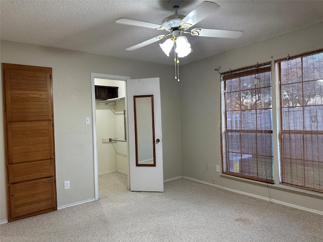 unfurnished bedroom with light colored carpet, a textured ceiling, a spacious closet, and ceiling fan