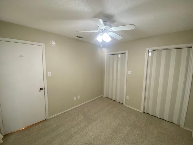 unfurnished bedroom with ceiling fan, a textured ceiling, light carpet, and two closets