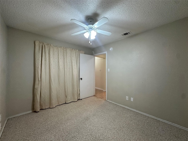 empty room with ceiling fan, light colored carpet, and a textured ceiling