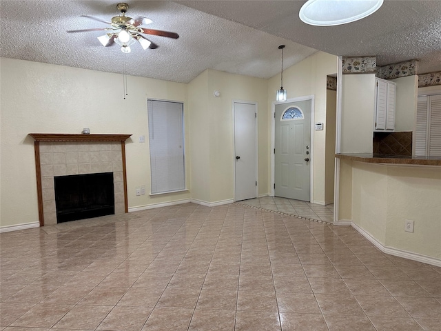 unfurnished living room with vaulted ceiling, a textured ceiling, a tiled fireplace, ceiling fan, and light tile patterned flooring