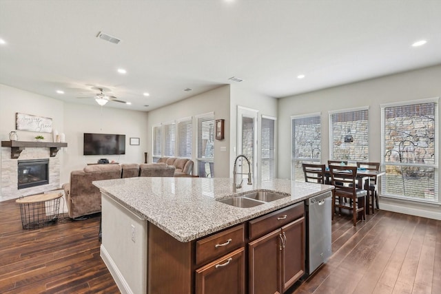 kitchen featuring stainless steel dishwasher, dark hardwood / wood-style flooring, sink, a fireplace, and a kitchen island with sink