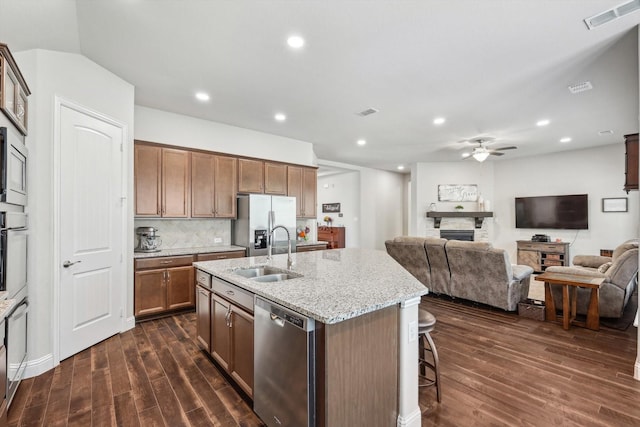 kitchen with sink, a center island with sink, stainless steel appliances, and a stone fireplace