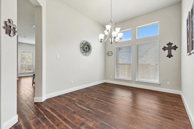 empty room with plenty of natural light, dark hardwood / wood-style floors, and a notable chandelier