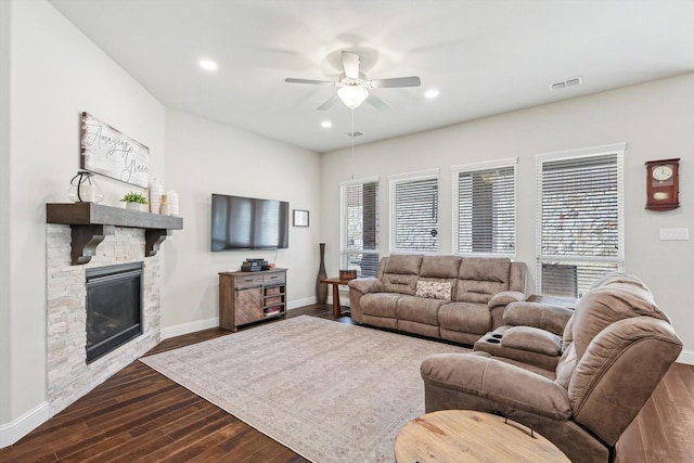 living room featuring ceiling fan, a stone fireplace, and dark wood-type flooring