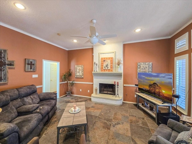 living room with a large fireplace, ceiling fan, ornamental molding, and a textured ceiling