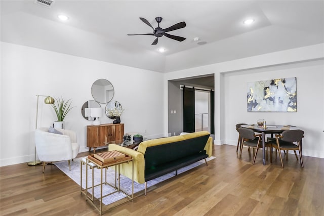 living room featuring ceiling fan, wood-type flooring, a tray ceiling, and a barn door