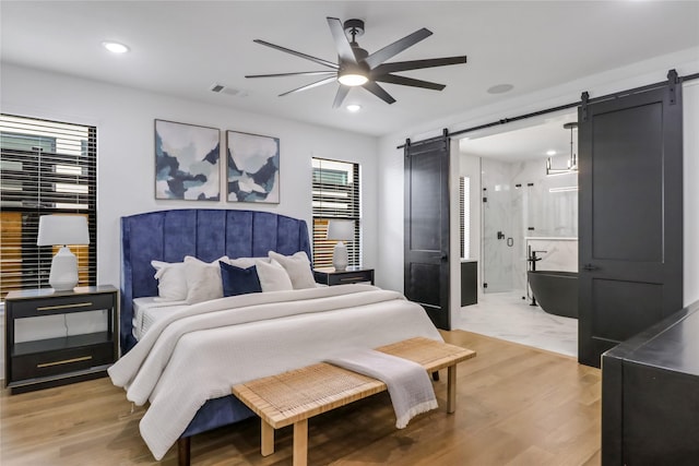 bedroom with ceiling fan, a barn door, and light hardwood / wood-style floors