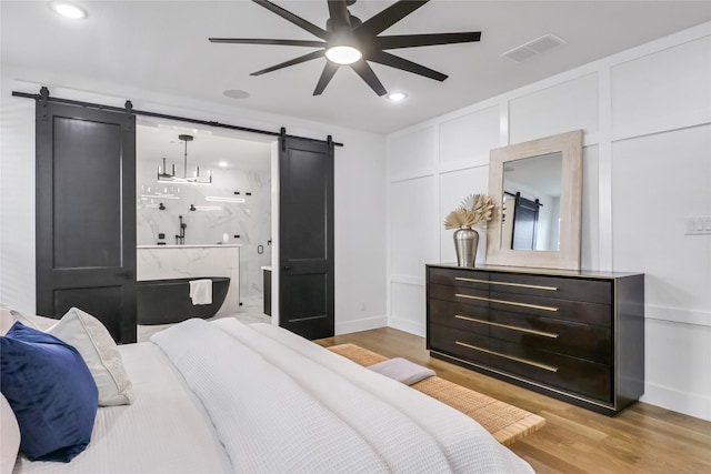 bedroom featuring light wood-type flooring, ceiling fan, and a barn door