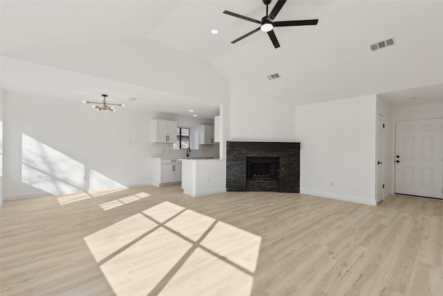 unfurnished living room featuring sink, light wood-type flooring, a stone fireplace, ceiling fan with notable chandelier, and lofted ceiling